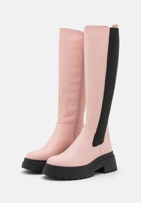 Bottes hauteur genou en cuir synthétique rose avec panneaux latéraux noirs élastiques et semelles épaisses en caoutchouc noir. Texture lisse, détails minimalistes.
