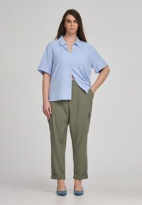 Camicia azzurro chiaro a maniche corte con bottoni, pantaloni tapered verde oliva con tasche cargo e tacchi blu. Tessuto morbido, vestibilità rilassata.