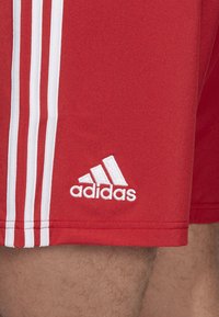 Rote Sportshorts aus leichtem Stoff, mit drei weißen Streifen an der Seite und einem eingestickten weißen Adidas-Logo.