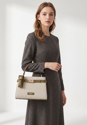 Jeune femme en robe grise à manches longues tenant un sac à main beige et olive avec une petite pochette attachée.