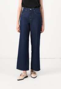 Δημιουργικά τζιν παντελόνια με φαρδιά πόδια σε σκούρο μπλε χρώμα, υψηλή μέση, φινιρισμένα με μπροστινές τσέπες και κλασικό κλείσιμο με κουμπί. Υφή �υφάσματος με ραμμένα αξεσουάρ.