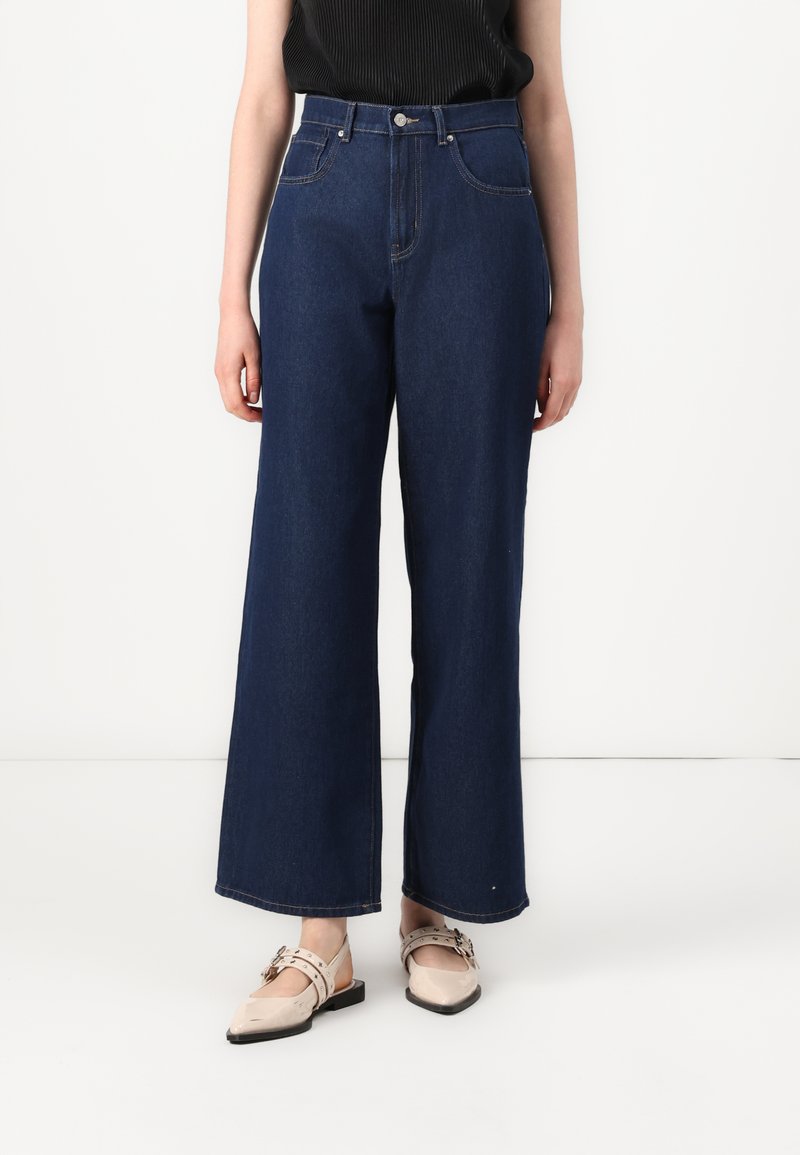 Δημιουργικά τζιν παντελόνια με φαρδιά πόδια σε σκούρο μπλε χρώμα, υψηλή μέση, φινιρισμένα με μπροστινές τσέπες και κλασικό κλείσιμο με κουμπί. Υφή υφάσματος με ραμμένα αξεσουάρ.