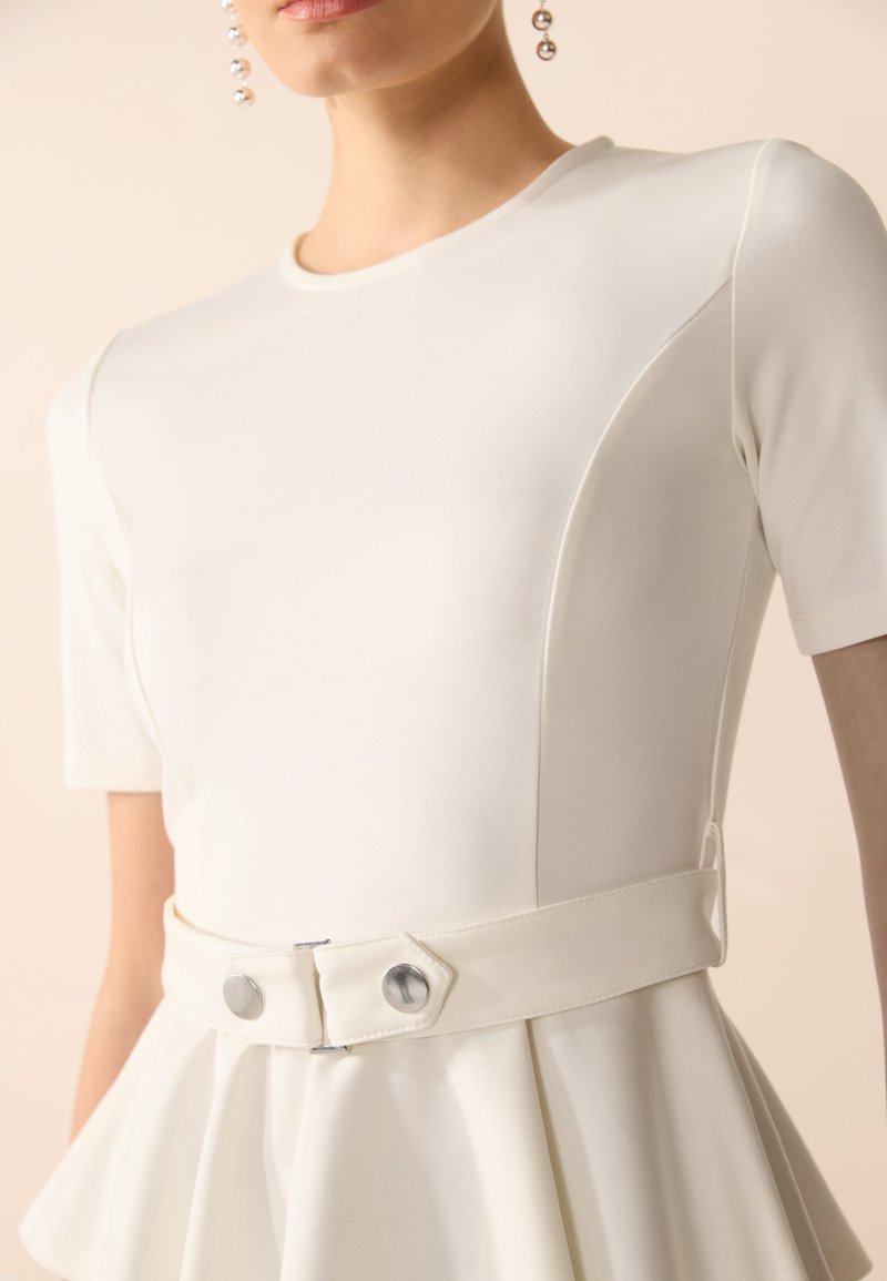 Weißes Kleid mit kurzen Ärmeln, das einen taillierten Oberteil und einen ausgestellten Rock aufweist, akzentuiert durch einen glatten Gürtel mit metallischen Knöpfen. Weicher Stoff.