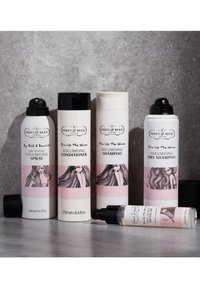 Vier haarverzorgingsproducten op een grijze ondergrond: een witte spuitbus, een zwarte conditioner, een witte shampoo-fles en een heldere olie met een zwarte dop.