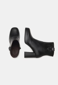 Schwarze Stiefeletten mit kräftigen Blockabsätzen, glattem Leder, abgerundetem Zehenbereich, dekorativem Kettendetail am Knöchel und seitlichem Reißverschluss.