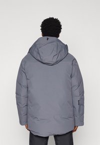 Veste matelassée grise avec capuche, présentant une texture lisse, des poignets élastiques et des accents de logo au dos et sur la manche.