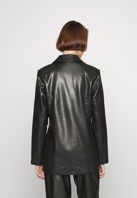 Czarna skórzana marynarka o strukturalnym kroju, z wyciętymi klapami i zapinanymi na guziki mankietami. Gładka tekstura i dopasowany fason. Widok od tyłu.