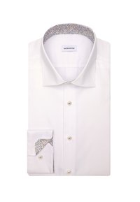 Chemise blanche pliée avec des détails floraux à l'intérieur du col et des poignets, avec des boutons blancs sur le devant et aux poignets.