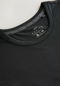T-shirt de sport noir respirant avec encolure ronde, étiquette intérieure indiquant "Next Active" et taille moyenne, et un ruban intérieur à motifs au col.