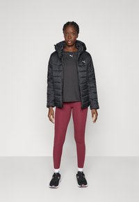 Doudoune noire avec capuche, haut gris, leggings bordeaux et sneakers noires. Présente des accents de logo et un design ajusté.