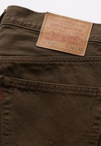 El bolsillo trasero de unos vaqueros Levi's 501 marrones con etiqueta de cuero que muestra la talla W32 L32 y la etiqueta roja de Levi's en la costura.