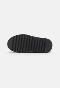Talpa de sneaker din cauciuc negru cu striații orizontale, vârf rotunjit și textură netedă. Prezintă branding minim și un design cu toc plat.