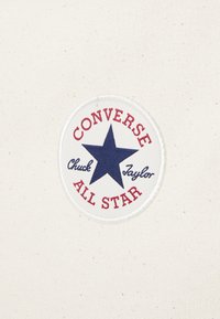 Pezza di tessuto bianco con un logo rotondo che presenta una stella azzurra e il testo rosso che legge "CONVERSE" e "Chuck Taylor" sopra "ALL STAR."