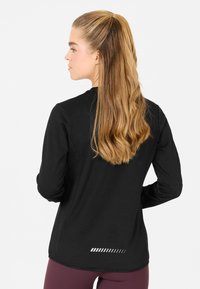 Schwarzes Longsleeve-Sportshirt mit strukturiertem Finish, das an der Rückseite einen gestreiften Akzent und eine lockere Passform aufweist.