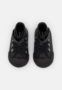 Para małych czarnych sneakerów wysokich z czarnymi sznurówkami i gumowymi podeszwami, widocznych z góry na białym tle.