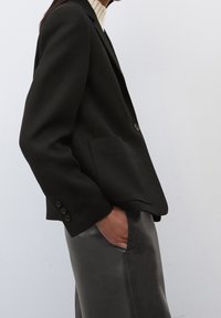 Blazer noir à coupe ajustée, avec une fermeture à un bouton et deux poches avant, associé à un pantalon en cuir noir élégant.