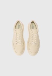 Baskets couleur crème avec un dessus en cuir lisse, bout arrondi et accents roses au niveau du col, dotées de lacets plats et d'une semelle rembourrée.