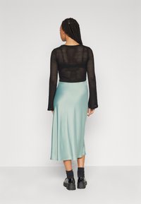 Svart strikket topp med lange ermer, kombinert med et mintgrønt sateng midi-skjørt som har en glatt tekstur og en tettsittende midje. Svart plattformsko.