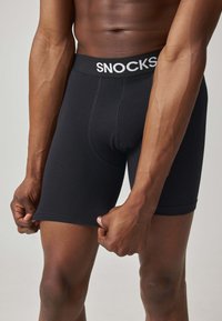 Zwarte boxershorts met een strakke pasvorm, voorzien van een brede elastische tailleband met het 'SNOCKS' logo. Gladde katoenstof, geen zichtbare patronen.