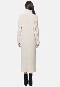 Strick-Kleid mit Rollkragen in Cremefarbe, vertikaler Rippung, langen Ärmeln und lässiger Passform, bis zur Mitte der Waden reichend, kombiniert mit schwarzen Plateaustiefeln.