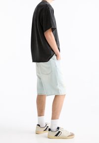 T-shirt noir surdimensionné, shorts en denim déchirés bleu clair, chaussettes blanches, baskets beiges avec des accents bleu marine ; présenté en vue de profil.