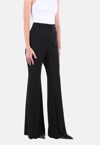 Pantaloni neri svasati realizzati in tessuto liscio, con vita alta, tasche laterali e una silhouette su misura che arriva fino a terra.