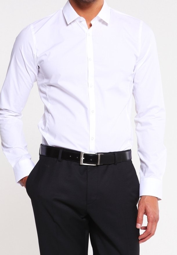Witte langarmige overhemd met een button-down kraag, gecombineerd met zwarte broek en een zwarte riem met een zilveren gesp.