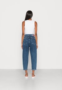 Blauwe denim jeans met hoge taille en losse pasvorm, met een vervaagde afwerking, voorzien van achterzakken en een contrasterend label op de tailleband. Gecombineerd met een wit tanktop.
