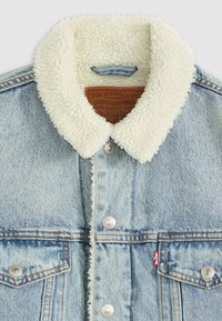 Jeansjack in lichtblauwe kleur, met een fluffy witte schapenwollen kraag, zilveren drukknoopsluitingen en een rode tabaccent op de linkerzak.