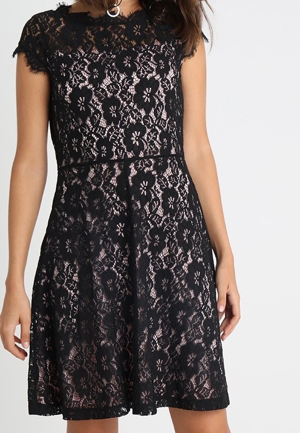 Schwarzes Spitzenkleid mit tailliertem Oberteil und ausgestelltem Rock, mit Blumenmustern und einer gewellten Ausschnittkante. Strukturierter Spitzenüberzug.