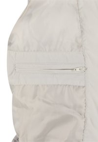 Lysegråt dunjakke stof med en glat tekstur, med en lynlåslomme på siden og syningsdetaljer langs sømmene.