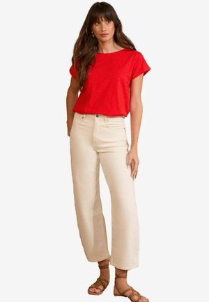 T-shirt rouge à manches courtes associé à un jean écru à jambes larges. La tenue est complétée par des sandales à lanières brun clair.