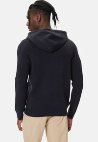 Felpa con cappuccio in maglia blu navy con finitura strutturata, dotata di cappuccio con coulisse e maniche lunghe, abbinata a pantaloni beige chiaro.