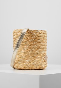 Borsa a secchiello in paglia intrecciata con una tracolla metallica, caratterizzata da una texture liscia e un accento in metallo logo rotondo sul lato.