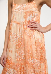 Rochie cu imprimeu portocalie, realizată dintr-un material ușor, cu bretele subțiri și un design stratificat, decorată cu motive florale și paisley.