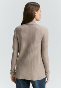 Beige Rippstrickpullover mit langen Ärmeln, lockerer Passform, subtiler Textur und leicht verlängertem Saum hinten. Baumwollmischung.