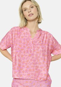 Blusa a maniche corte di colore rosa con stampa leopardata arancione, dotata di chiusura a metà bottoni e vestibilità rilassata. Tessuto morbido e materiale leggero.