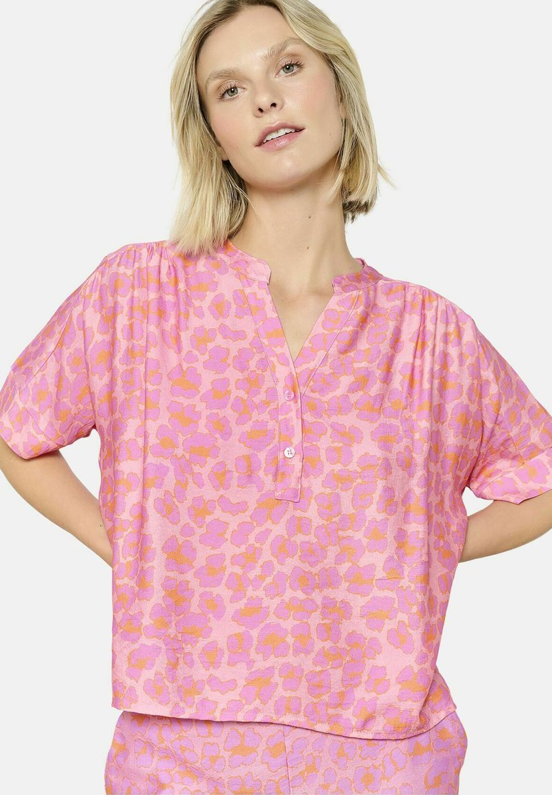 Blusa a maniche corte di colore rosa con stampa leopardata arancione, dotata di chiusura a metà bottoni e vestibilità rilassata. Tessuto morbido e materiale leggero.