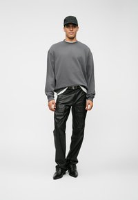 Γκρι φούτερ, μαύροι ψεύτικοι δερμάτινοι παντελόνες και μαύρα παπούτσια. Το μοντέλο φοράει ένα μαύρο καπέλο, με χαλαρό σχέδιο και άνετη εφαρμογή.