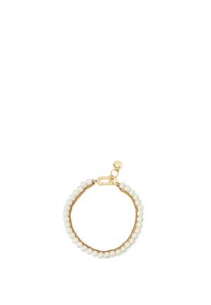 Bracelet chaîne en or avec une rangée de perles blanches et un fermoir rond en or orné d'une petite étiquette circulaire.