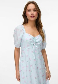 Robe bleu clair avec imprimé floral, manches bouffantes, décolleté carré et détail froncé au centre avec un noeud. Tissu doux et texturé.