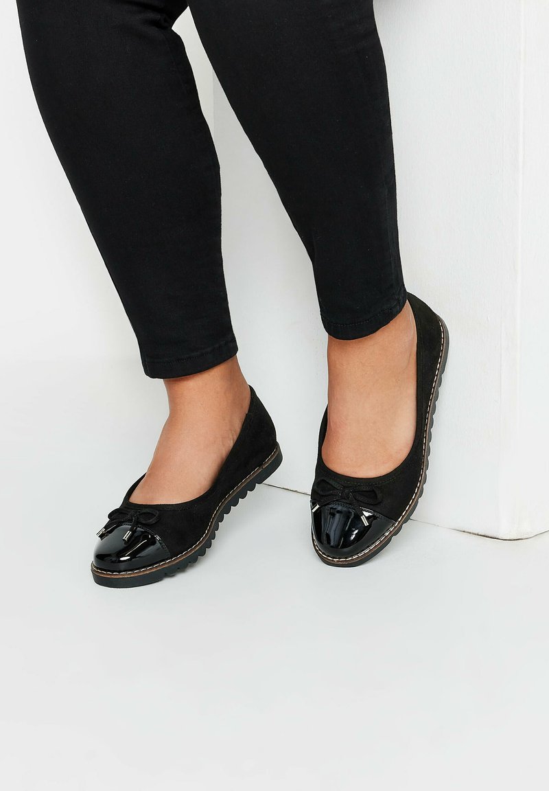 Svarta mocka balettskor med en blanka svarta lacktå, med en rosettdetalj och kontrasterande sömnad längs sulan. Texturerad gummi sula.