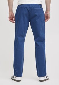 Niebieskie bawełniane spodnie o prostym kroju, z tylną kieszenią i lekką teksturą, noszone z białymi i czarnymi paskowanymi sandałami.