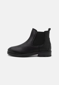 Botas de cuero negro hasta el tobillo con paneles laterales elásticos, punta redondeada y tacón bajo. Presentan costuras visibles a lo largo de la suela y una asa en la parte posterior.