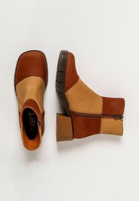 Botas de tobillo marrones y beige con un acabado texturizado, que presentan un cierre lateral con cremallera y un tacón cuadrado. La parte superior mezcla materiales lisos y de ante.
