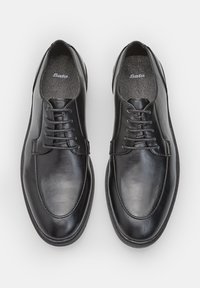 Chaussures en cuir noir au fini lisse, bout arrondi et design à lacets. Semelle intérieure grise visible, avec des détails de logo subtils.