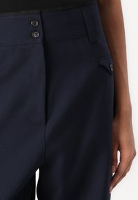 Pantalons ajustés bleu marine avec un devant plat, fermeture à boutons-pression et une poche latérale avec des détails de couture subtils.