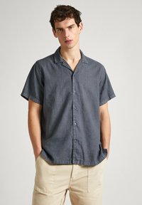 Short-sleeve button-up shirt in dark gray fabric, featuring a notched collar and subtle texture, paired with beige trousers.