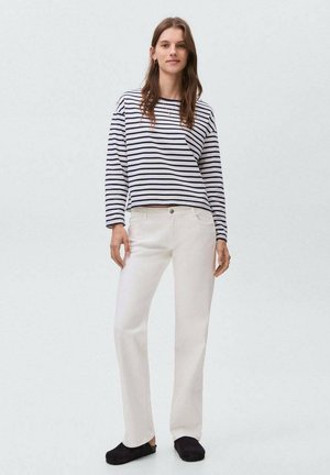 Maglietta a maniche lunghe a righe in blu navy e bianco, abbinata a pantaloni bianchi a gamba dritta. L'outfit ha una vestibilità comoda ed è completato da ballerine nere.