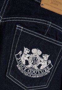 Σκούρο μπλε τζιν τσέπη με λευκό κεντημένο λογότυπο Juicy Couture και κείμενο, καθώς και δερμάτινη ετικέτα πάνω από την τσέπη.
